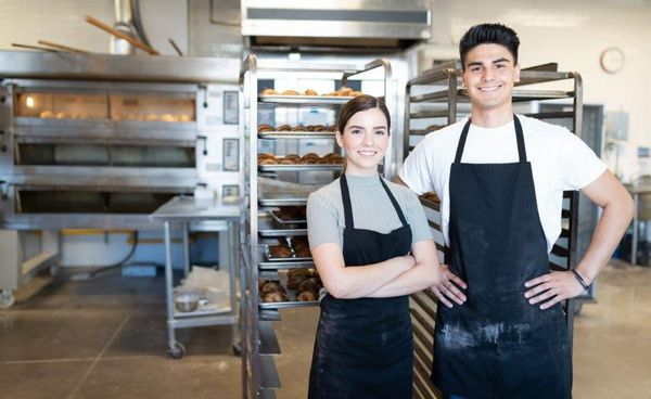 Zwei Auszubildende stehen in einer Bäckerei und blicken in die Kamera.